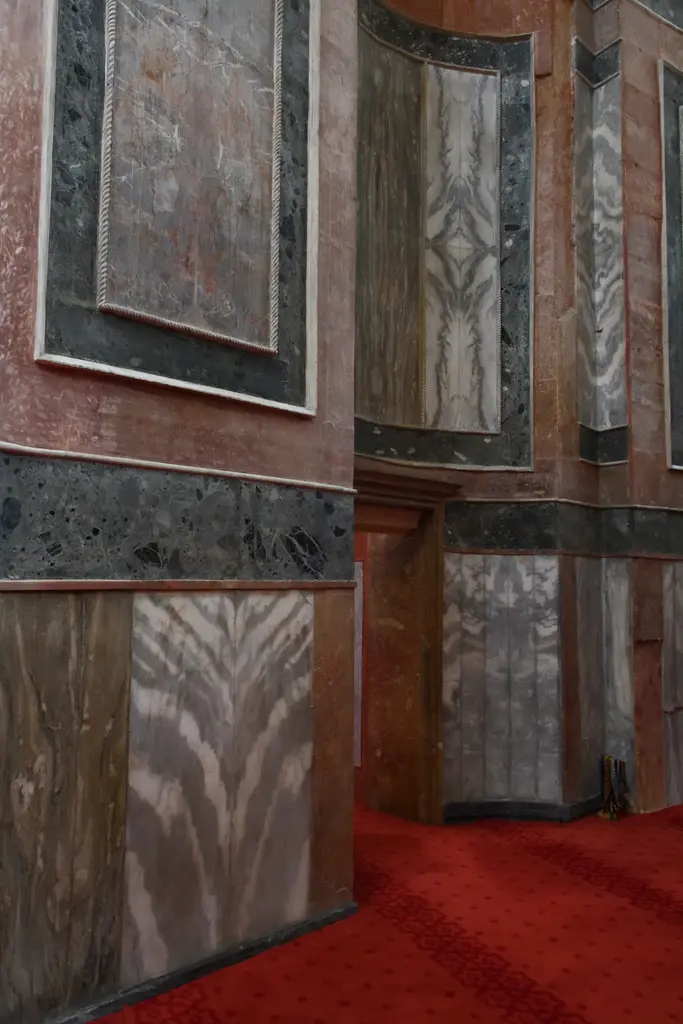 Zeyrek Camii'nde duvar kaplaması; dikdörtgen çerçeveler içinde gri, pembe ve koyu yeşil damarlı mermer levhalar, altta kırmızı halı, üstte beyaz silme.