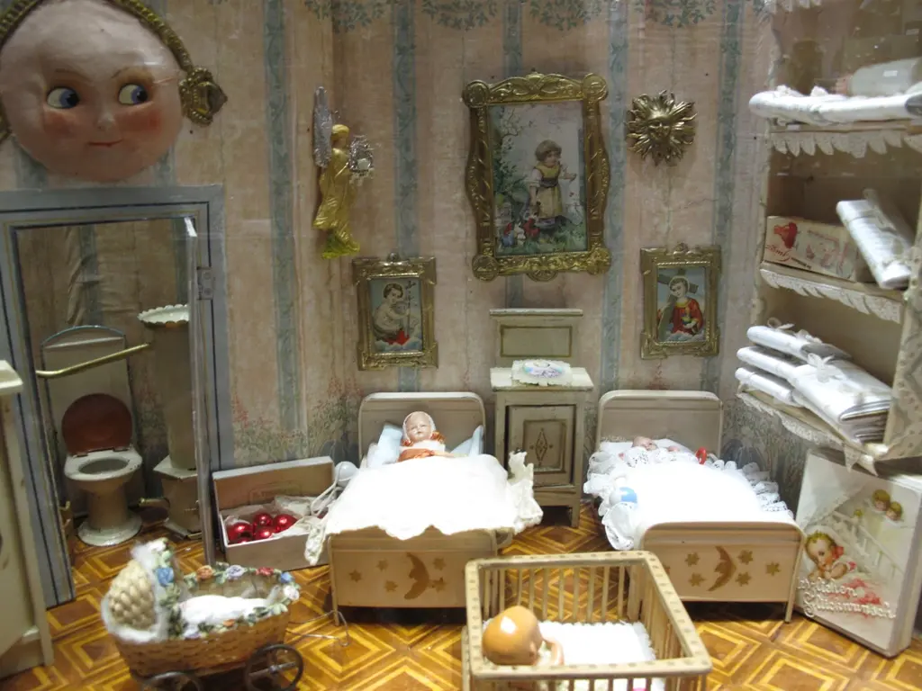 İstanbul Oyuncak Müzesi'nde bebek evi yatak odası; desenli duvar kâğıdı, minik yataklar, beşik, çerçeveli resimler ve ay yüzlü lamba.