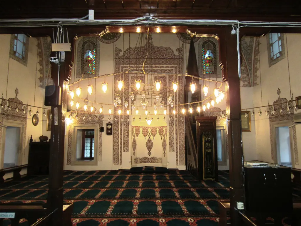 Firuz Ağa Camii'nin harimi; yanan avize halkaları, ahşap direkler, halı zemin ve karşıda mihrap ile minber.