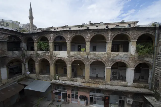 Fatih'te Büyük Yeni Han'ın avlusu; zemin katta dükkânlar, üstünde iki sıra taş ve tuğla almaşık revak, arkada bir minare.