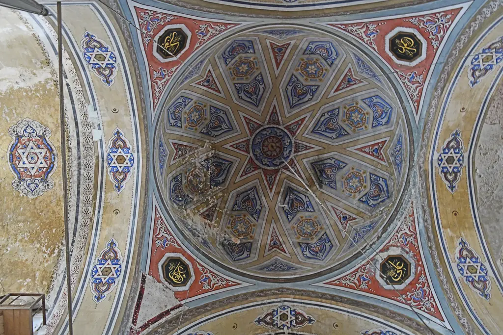 Gül Camii'nin kubbesi tam aşağıdan; mavi, koyu sarı ve kırmızı renklerle çizilmiş çok köşeli yıldız kompozisyonu, rozetler ve sıva dökülmeleri.