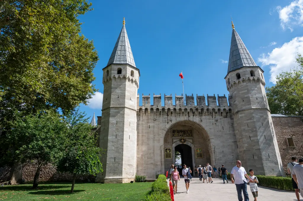 Sultanahmet'te Topkapı Sarayı'nın Babüsselam kapısı; iki konik külahlı kule arasındaki kemerli taş giriş, mazgallı duvarlar ve kapıya yürüyen ziyaretçiler.