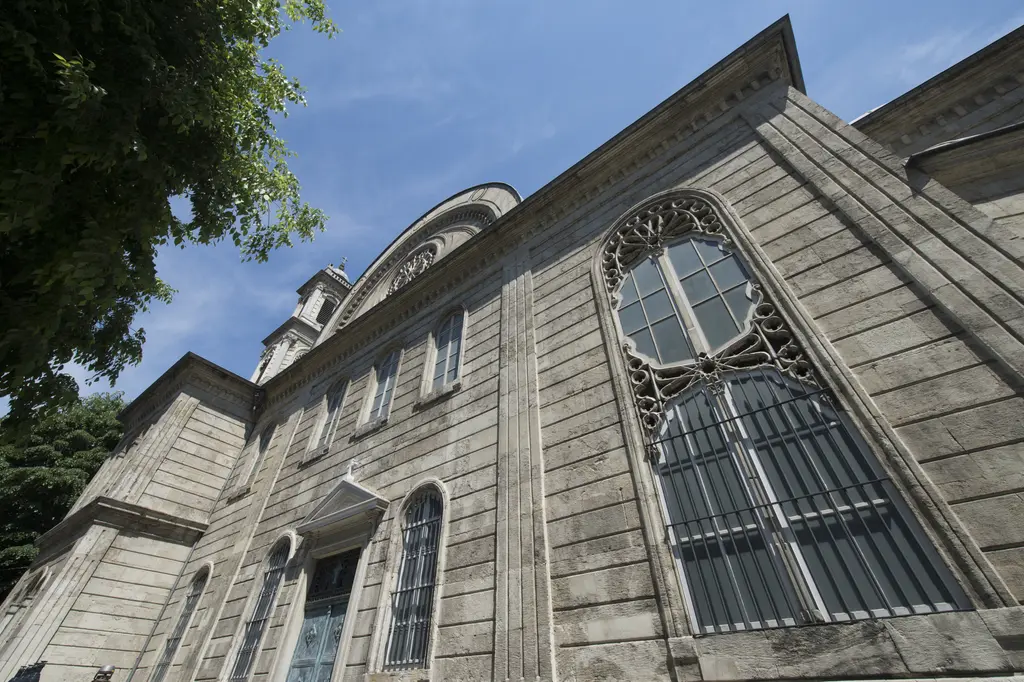 Aya Triada Kilisesi'nin yan duvarı; kesme taş yüzey, sivri ve yuvarlak kemerli pencereler, silmeler ve mavi gökyüzü.
