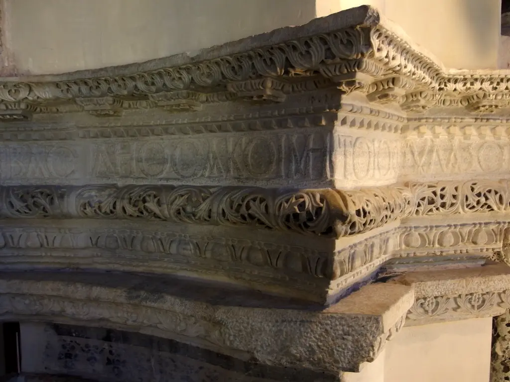 Küçük Ayasofya Camii'nde kitabe frizinin köşesi; mermer arşitrav üzerinde okunaklı Yunanca kapital harfler, üstünde ve altında yumurta ok, inci dizisi ve delik işi asma dalı bantları.