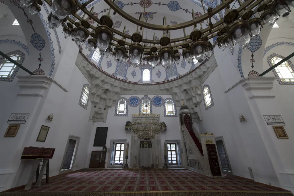 Gazi Atik Ali Paşa Camii'nin harimi; yarım kubbe altında mihrap, sağda minber, kalem işli kemerler, halka avize ve kırmızı halı.