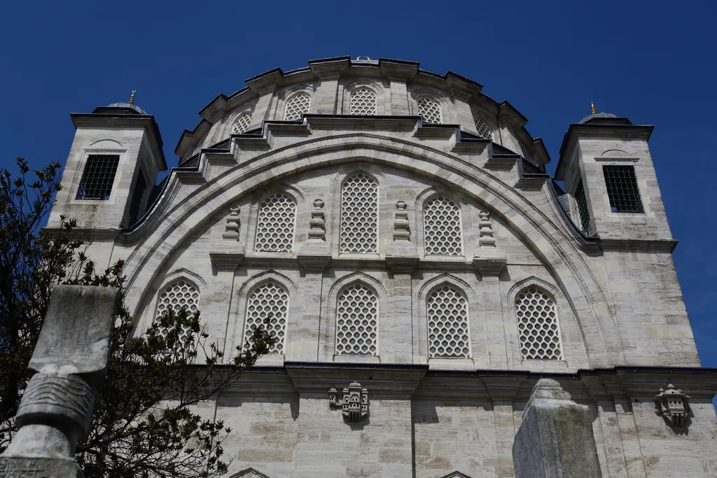 Ayazma Camii'nin yan cephesi; aşağıdan bakışla kemerli duvar, kafesli pencereler ve köşe kuleleri, koyu mavi gökyüzü.