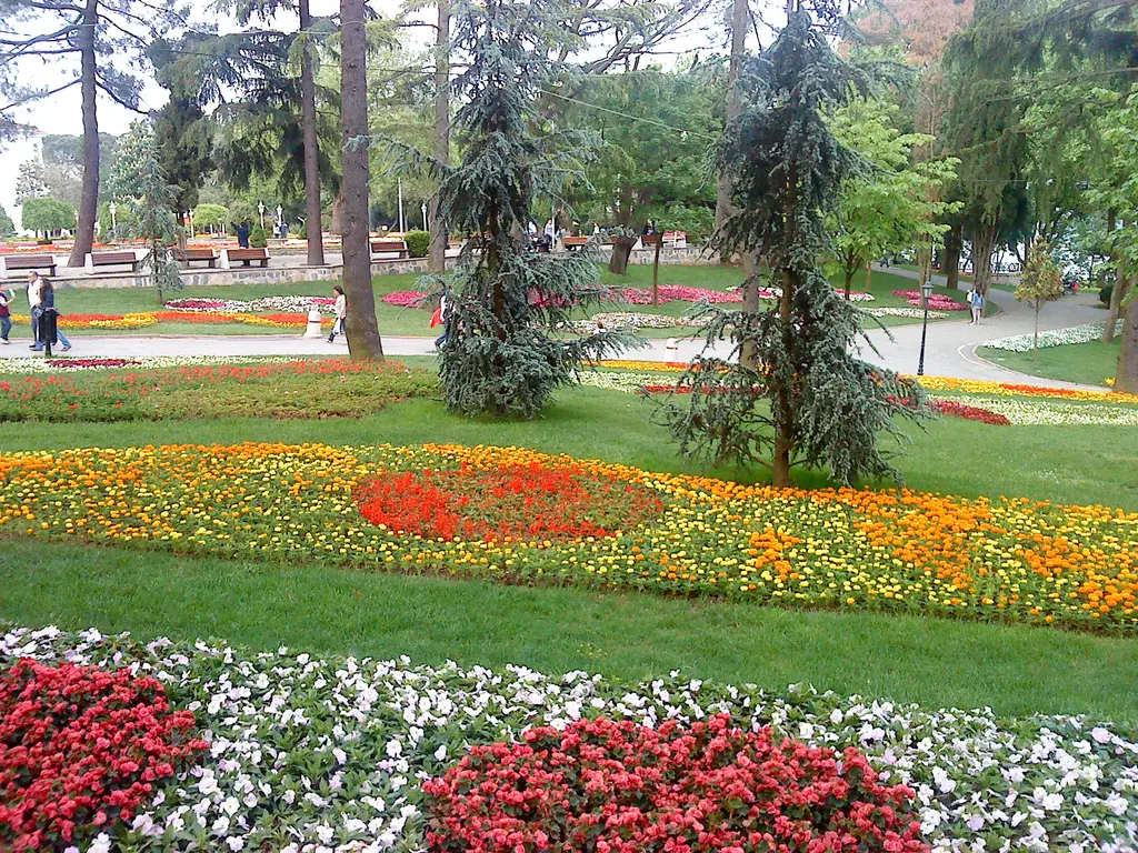 Emirgan Korusu'nda çiçek tarhları; turuncu ve kırmızı laleler, beyaz çiçekli şerit, mavi ladinler ve banklar.
