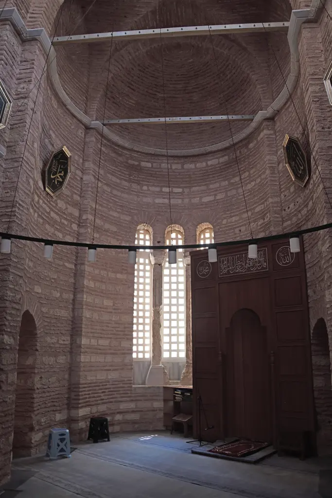 Fenari İsa Camii'nde kıble ucu; yarım kubbeli tuğla apsis, üç ince mermer şebekeli pencere, sağda hat kuşaklı koyu ahşap bölme ve içindeki kemerli mihrap nişi.