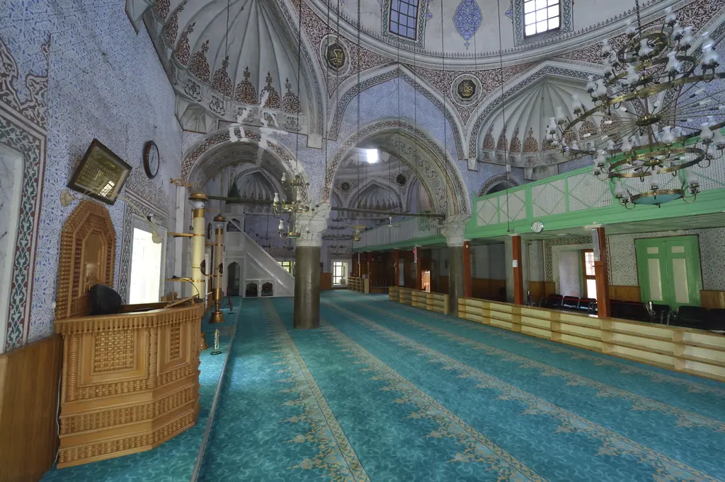 Haseki Sultan Camii'nde harimi ikiye ayıran kemer dizisi; beyaz başlıklı sütunlar, yeşil ahşap mahfiller ve turkuaz halı.