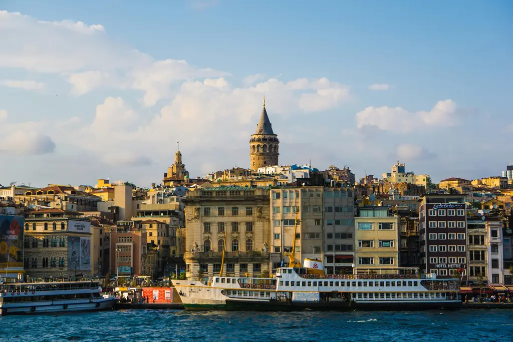 Denizden Karaköy kıyısı; önde bağlı şehir hattı vapurları, arkada taş cepheli eski banka ve han binaları, tepede Galata Kulesi.