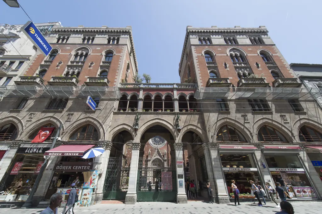 İstiklal Caddesi'nde Sent Antuan apartmanları; kırmızı tuğla ve taş cepheli iki blok, kemerli zemin kat dükkânları ve ortada avluya açılan kapı.