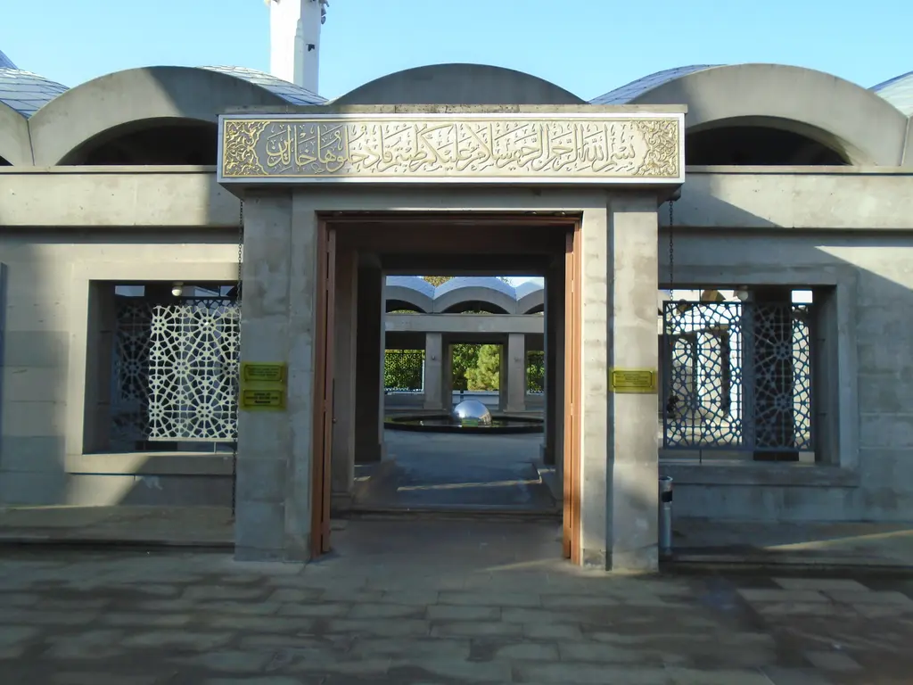 Şakirin Camii'nin avlu kapısı; üstünde altın yazılı kuşak taşıyan taş çerçeve, iki yanda kafesli pencereler ve revaklar.