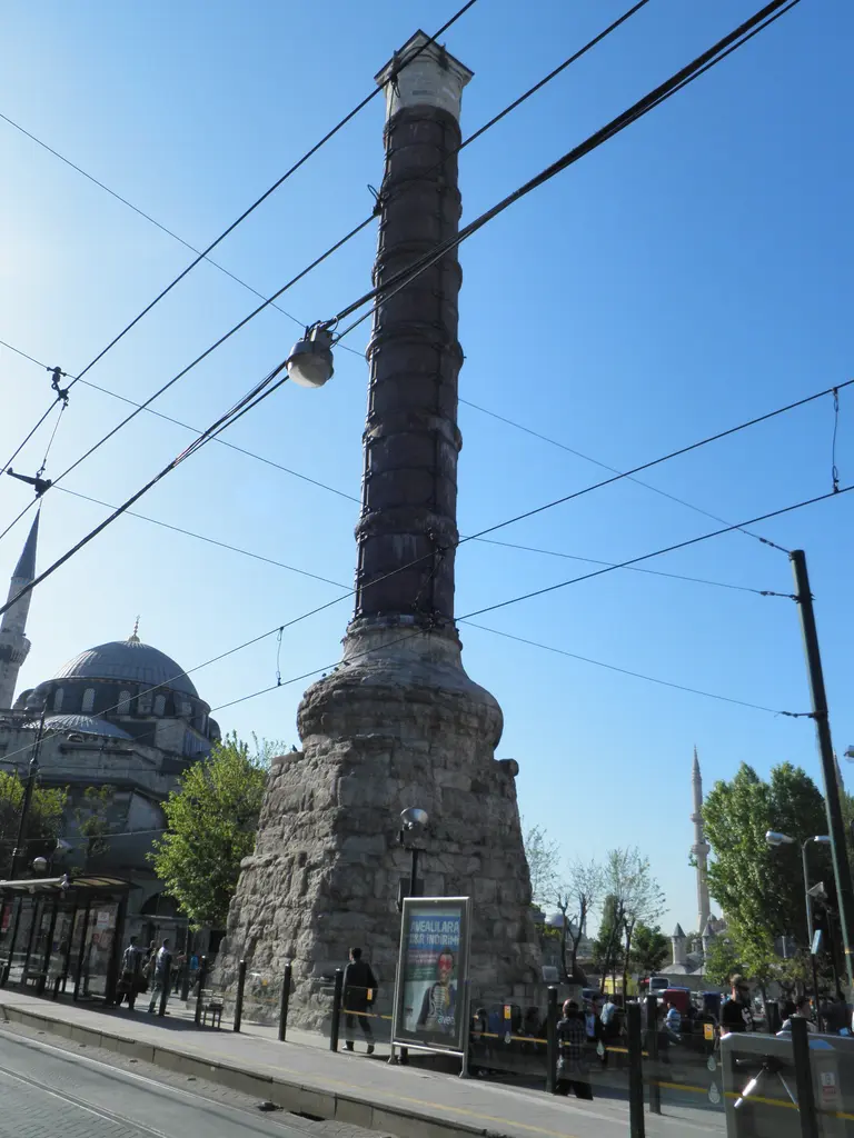 Çemberlitaş'ta sütun ile tramvay hattı; gövdenin önünden geçen katener telleri, altta peron ve arkada açık gökyüzü.