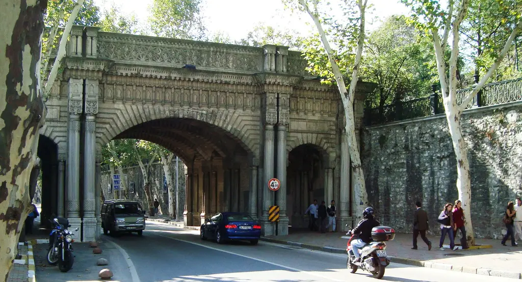 Çırağan Caddesi'nde sarayın geçidi; caddenin üstünden geçen kemerli taş köprü, altında araçlar ve yayalar, iki yanda ağaçlar.