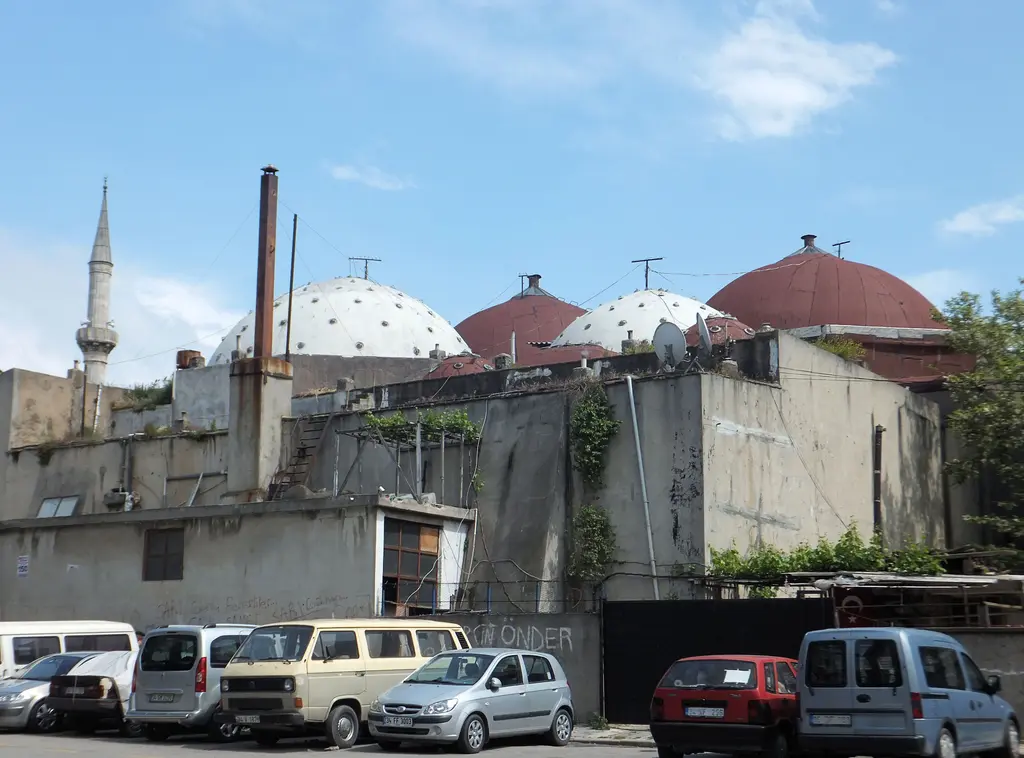 Çinili Hamam'ın kubbeleri; beyaz ve kırmızı kubbeler, bacalar, önde eski binalar, arabalar ve arkada minare.