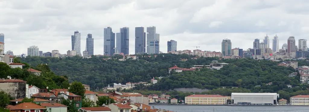 Kuzguncuk sırtlarından Yıldız Parkı; Boğaz'ın karşı kıyısında yeşil bir yamaç, ön planda evler, arkada Levent'in kuleleri.