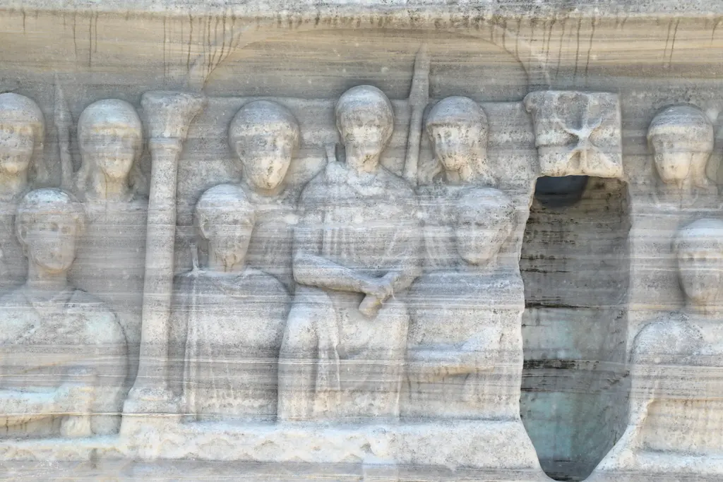 Dikilitaş kaidesinde imparator ve sarayı; ortada oturan figürler, iki yanda ayakta duran muhafızlar ve yüzeyde dikey bir yarık.