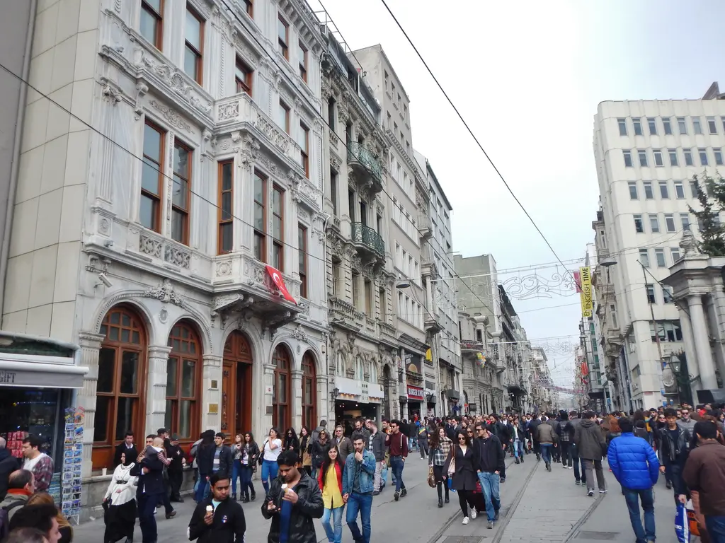 Galatasaray yakınında beyaz mermer cepheli eski postane binası; kemerli kapılar, bayraklı balkon ve önünden geçen kalabalık.