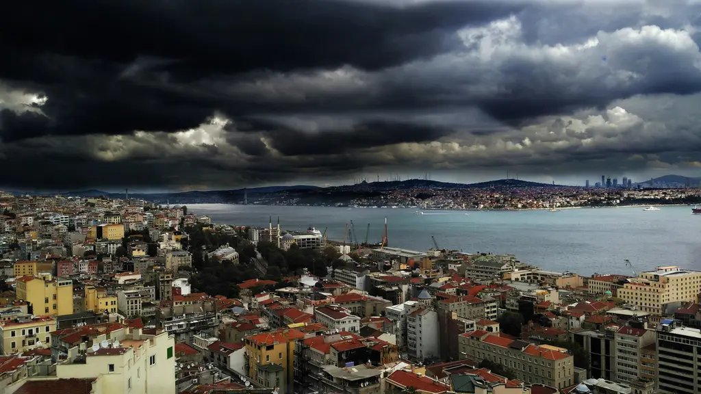Beyoğlu'nun yamaçlarından Boğaz; önde kırmızı kiremitli çatılar ve apartmanlar, ortada Boğaz'ın suyu, ufukta Anadolu yakası ve koyu fırtına bulutları.