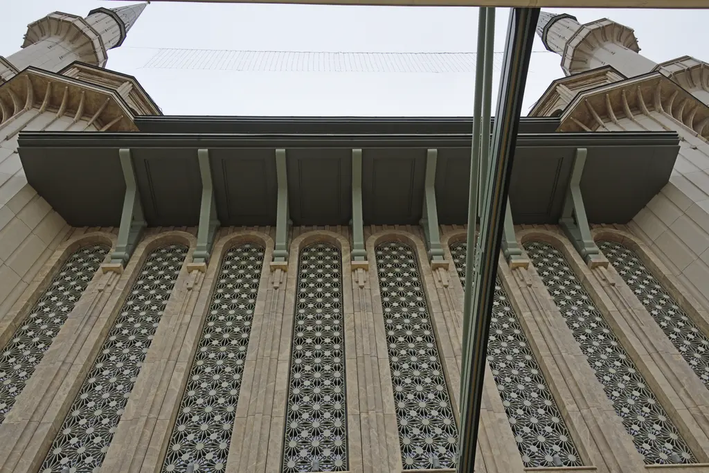 Taksim Camii'nin cephesi aşağıdan; geniş saçak ve konsolları, altında uzun kemerli pencereler ve yıldız desenli metal şebekeler.