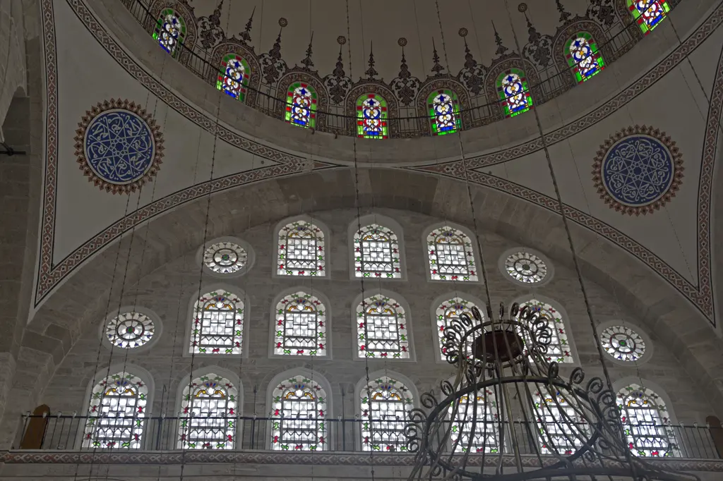 Mihrimah Sultan Camii'nin yan duvarı içeriden; üst üste sıralanan üç kat pencere, en üstte renkli vitraylar ve aydınlanmış duvar yüzeyi.