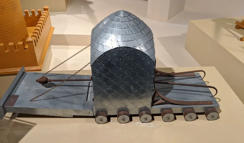 Zırhlı koçbaşı maketi; tekerlekli taban üstünde pullu metal kaplı kubbe biçimli örtü, önde uzanan koç direği ve arkada kale maketi.