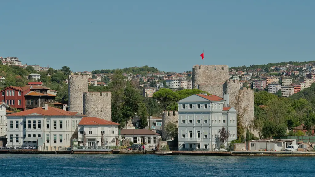 Denizden Anadolu Hisarı; kıyıdaki beyaz ve kırmızı yalıların ardında kuleler, iç kale ve yamaçtaki evler.