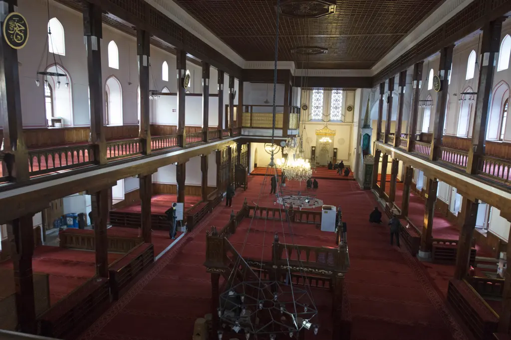 Arap Camii'nin içi; kırmızı halı, ahşap direkler, mahfiller ve ilerde avize çemberinin altında mihrap duvarı.