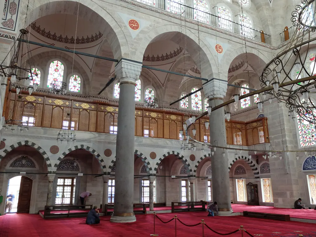 Mihrimah Sultan Camii'nde yan mahfil; kalın taş sütun, üstünde ahşap korkuluklu galeri, altta kemerli geçitler ve duvardaki pencere sırası.