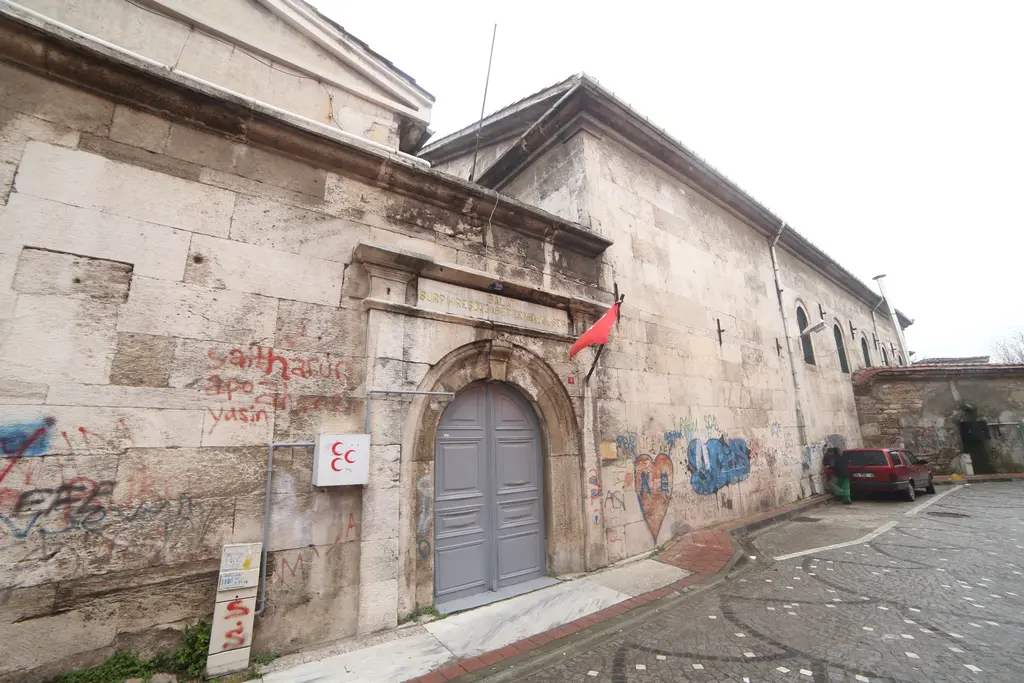 Surp Hreşdagabet Kilisesi'nin taş cephesi; kemerli gri kapı, Ermenice yazıtlı duvar, grafitiler ve dar sokak.