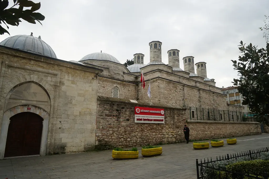 Haseki Hürrem Sultan İmareti; uzun kesme taş cephe, kubbeler ve bacalar, kapının yanında kırmızı bir tabela ve taş döşeli kaldırım.