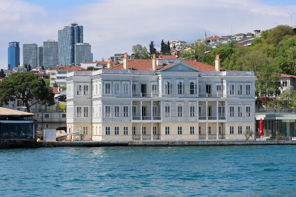 Boğaz'dan Fehime Sultan Yalısı; beyaz cepheli üç katlı yapı, kırmızı çatı, kıyı rıhtımı ve arkada gökdelenler.