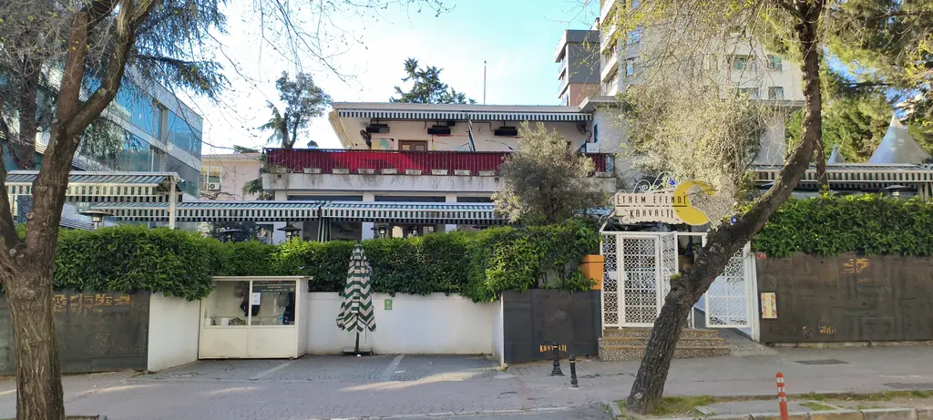 Bağdat Caddesi çevresinde Emin Onat Köşkü; ağaçların arasında beyaz cepheli köşk, önünde bahçe duvarı ve geniş kaldırım.