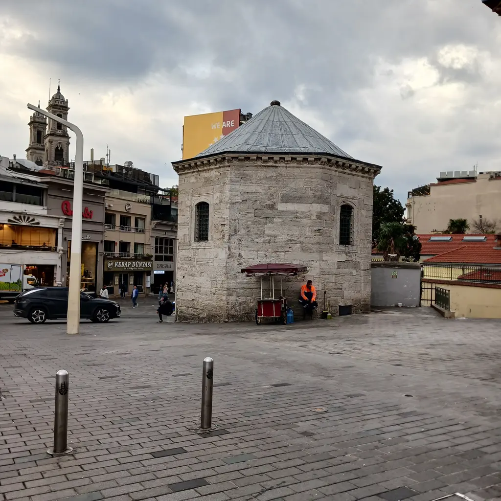 Taksim Meydanı'nda Taksim Maksemi; sekizgen kesme taş gövde, kurşun kaplı piramit çatı ve önünde taş döşeli alan.