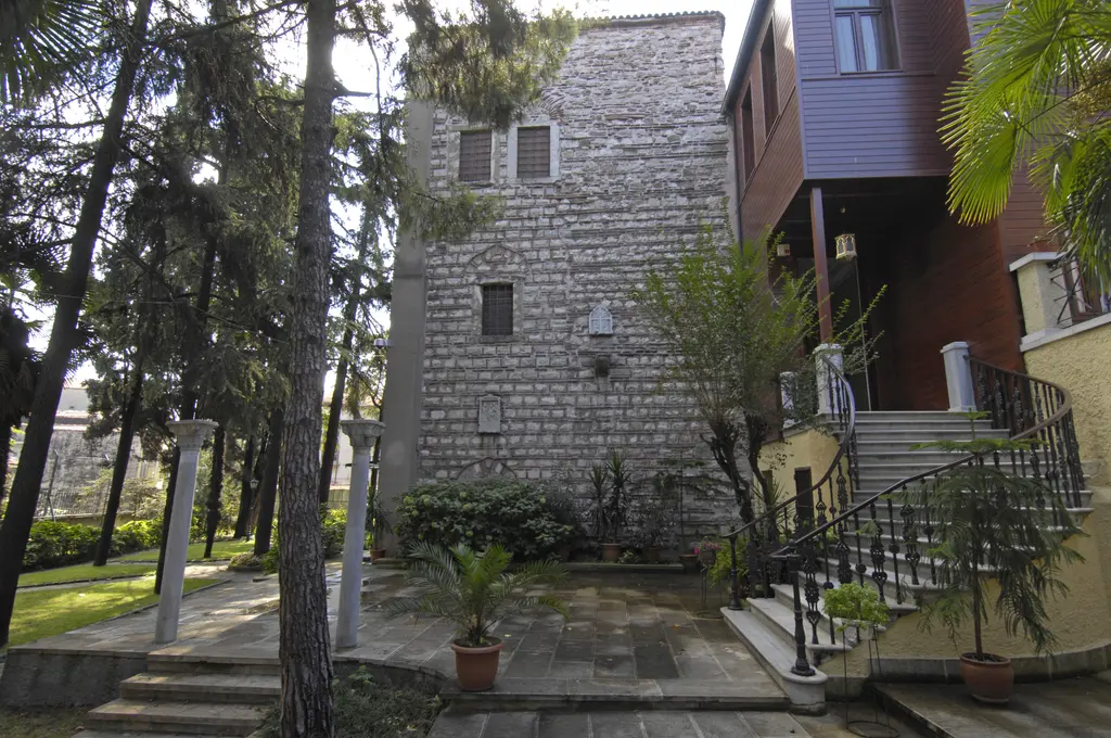 Patrikhane yerleşkesinde taş kule biçimli yapı; önünde bahçe, sütunlar, palmiye, çam ağaçları ve demir korkuluklu merdiven.