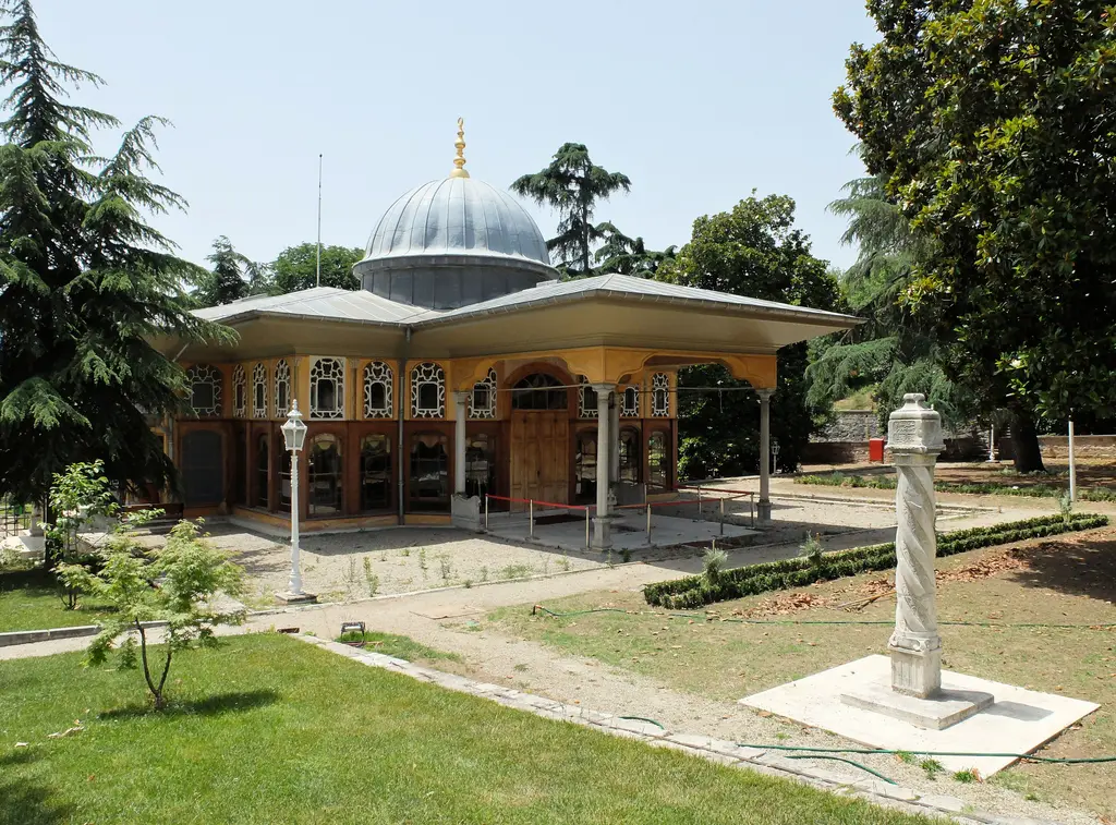 Aynalıkavak Kasrı'nın kara cephesi; geniş saçaklı sundurma, arkasında kubbe, bahçede beyaz bir nişan taşı ve çimenler.