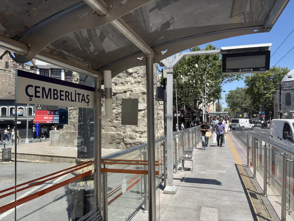 Çemberlitaş tramvay durağı; sundurmanın altında "ÇEMBERLİTAŞ" yazılı tabela, cam paravan ve arkasında sütunun taş kaidesi.