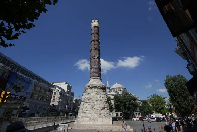 Çemberlitaş'ta Konstantin Sütunu; koyu kırmızı porfir gövde, gövdeyi saran demir çemberler, kaba taş kaide ve arkada mavi gökyüzü.