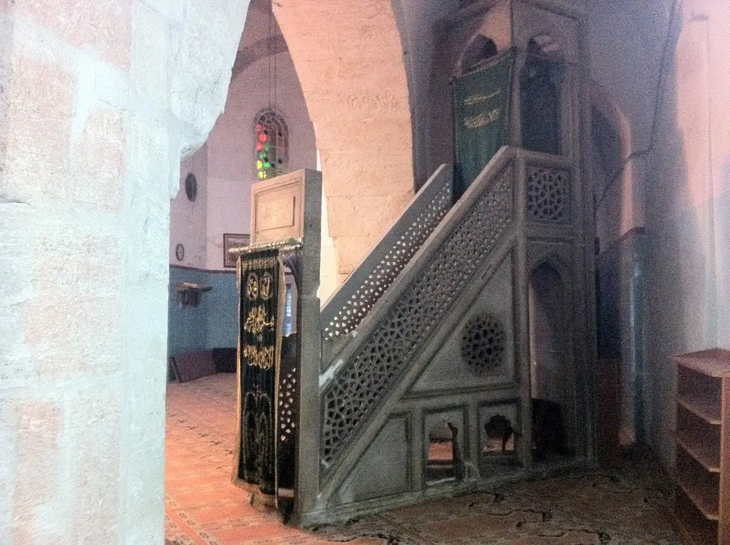 Fethiye Camii'nin cami bölümünde ahşap minber; sedef kakmalı yan aynalık, oymalı korkuluk, dar basamaklar ve arkasında pembe boyalı duvar.