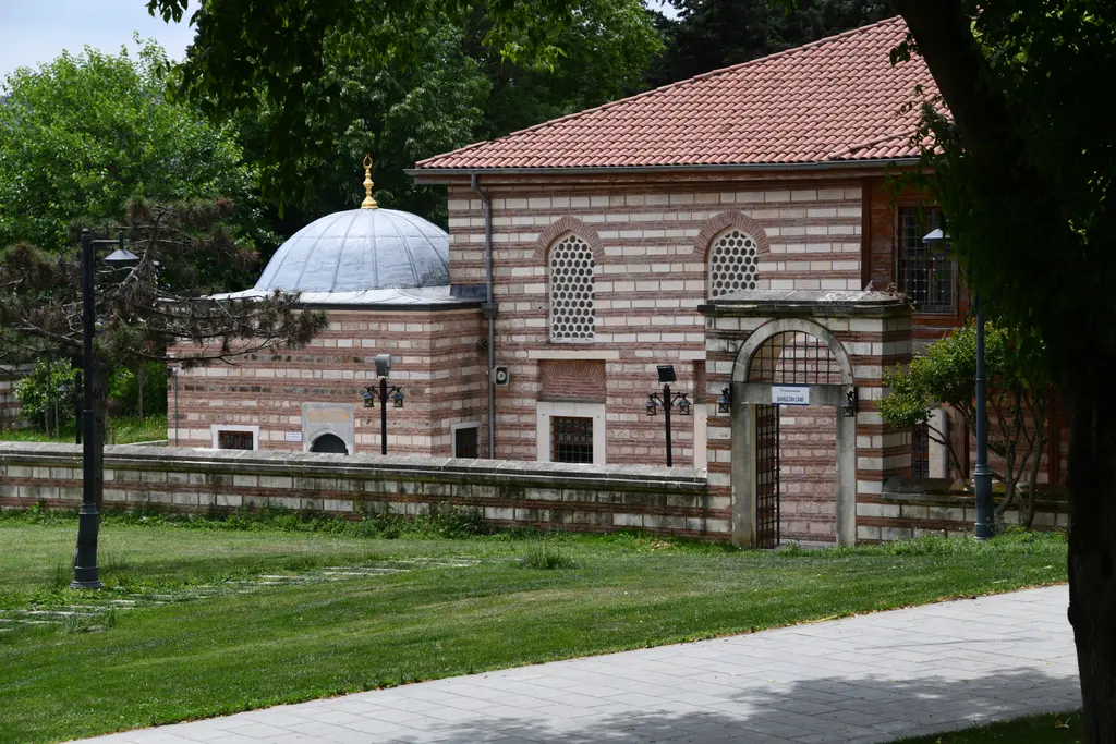 Şah Sultan Camii ve türbesi; kurşun kubbeli küçük türbe, kiremit çatılı cami, kemerli taş kapı ve önünde çimenlik.