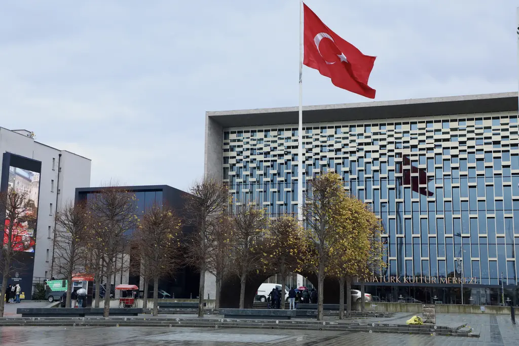 Taksim Meydanı'nda Atatürk Kültür Merkezi; ızgara desenli cam cephe, önünde sonbahar yapraklı ağaçlar ve dalgalanan büyük Türk bayrağı.