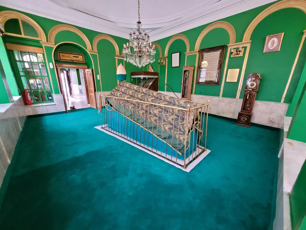 Karaca Ahmed Sultan Türbesi'nin içi; yeşil duvarlar, altın çerçeveli kemerler, avize ve pirinç parmaklıklı sanduka.