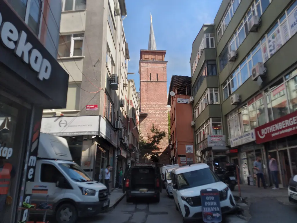 Perşembe Pazarı sokağından Arap Camii'nin minaresi; iki yanda dükkânlı binalar, ortada kare tuğla kule ve sivri külah.