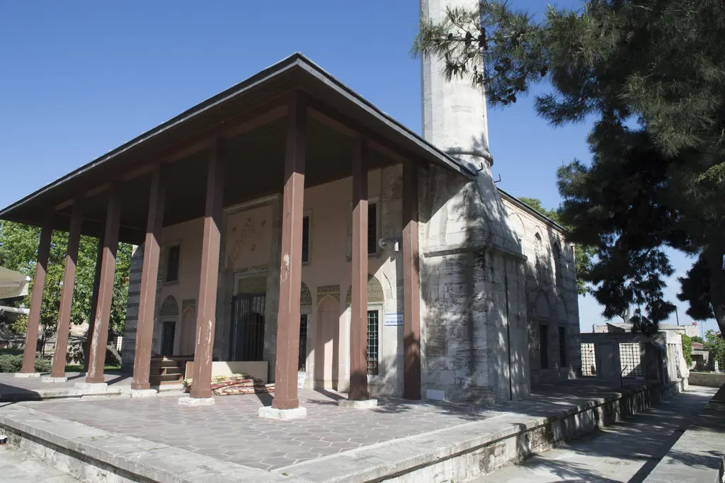Takkeci İbrahim Ağa Camii; ahşap direkli son cemaat yeri, taş gövde, yanda tek şerefeli minare ve avluda selviler.