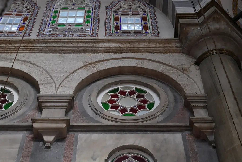 Laleli Camii'nde pencere ve duvar detayı; renkli camlı alçı pencereler, altında mermer kaplı duvar yüzeyi ve profilli silmeler.