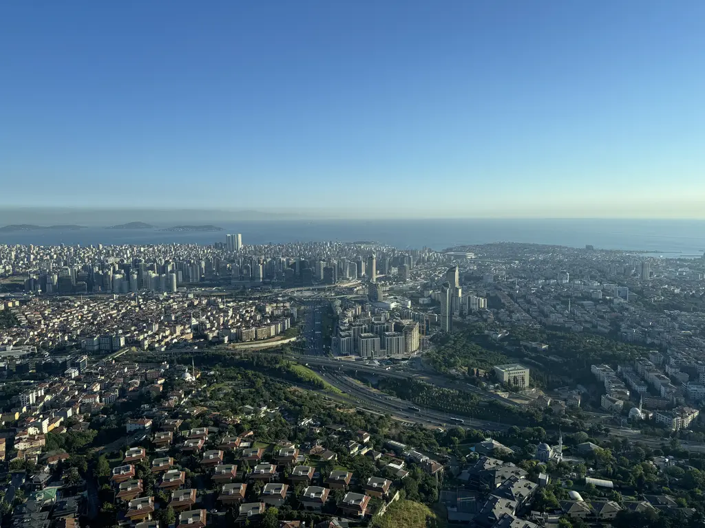 Çamlıca Kulesi'nden manzara; açık mavi gökyüzü, ufukta Marmara Denizi, yeşil alanlar ve yoğun yerleşim.