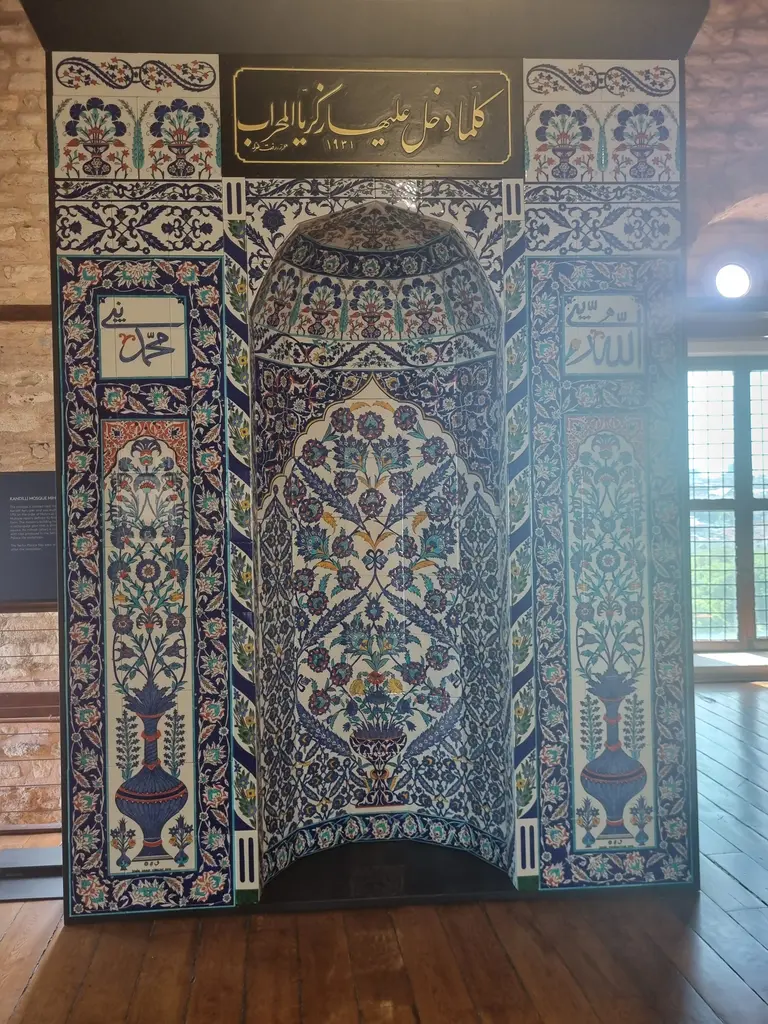 Çiniyle kaplı mihrap biçiminde pano; sivri kemerli alınlık, iki yanda burmalı sütunlar, bitkisel desenli karolar ve üstte kitabe kuşağı.