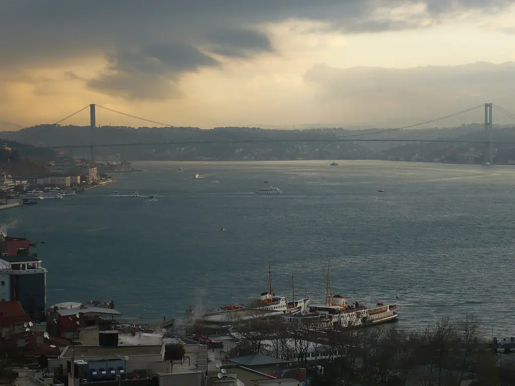 Cihangir'den Boğaz'a bakış; bulutlu gökyüzü altında gri su, kıyıda çatılar ve uzakta asma köprü.
