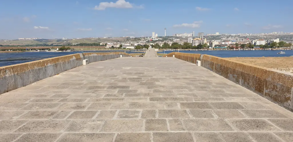 Kanuni Sultan Süleyman Köprüsü'nde yürüyüş yolu; geniş taş döşeme, iki yanda alçak korkuluklar ve uzakta şehir.