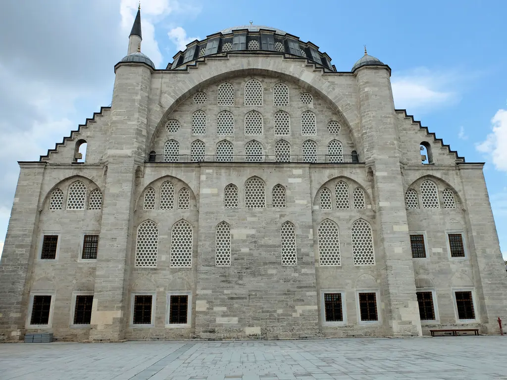 Mihrimah Sultan Camii'nin cephesi güneşli havada; kemerin içini dolduran üç sıra pencere, köşelerdeki ağırlık kuleleri ve mavi gökyüzünde yükselen kubbe.